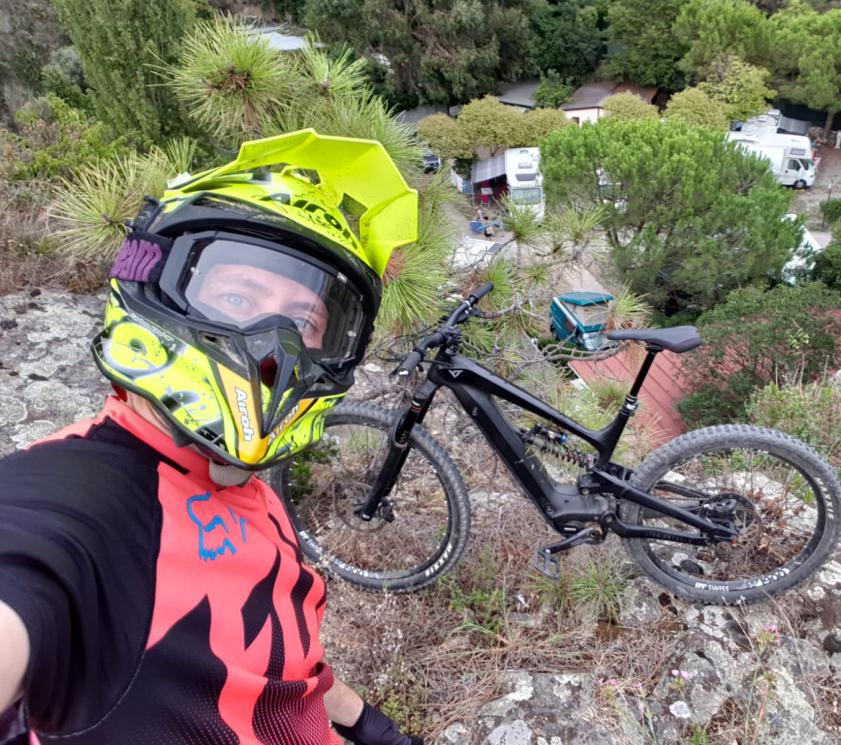 Ciclista con casco giallo e bici nera, vista su un campeggio.