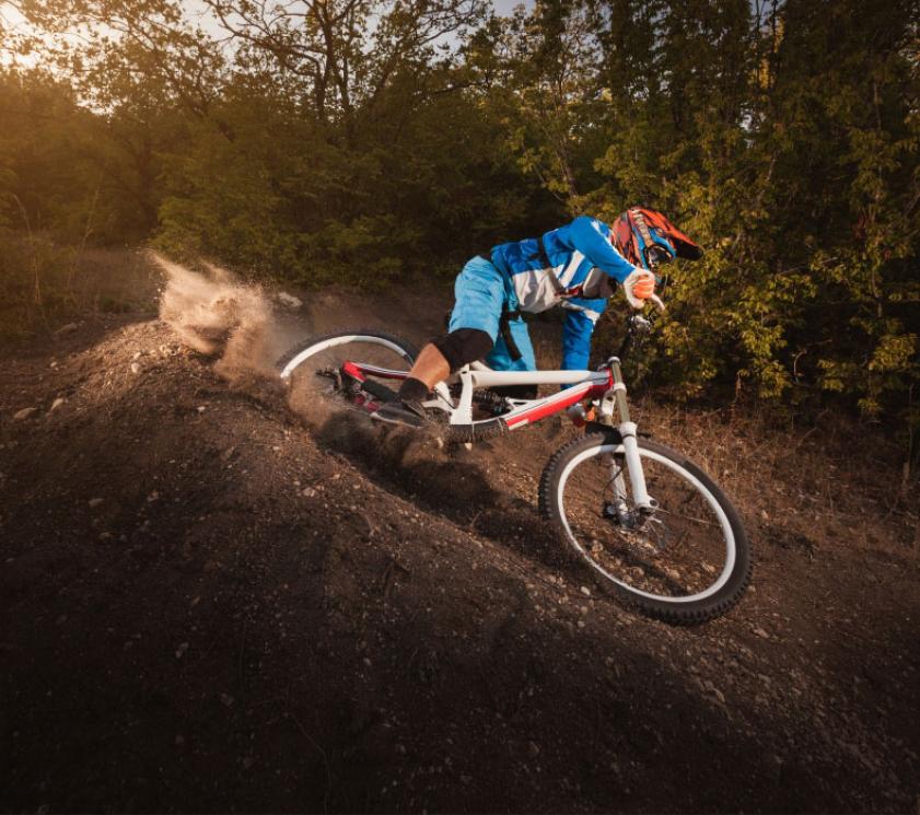 Ciclista in discesa su sentiero sterrato, sollevando polvere.